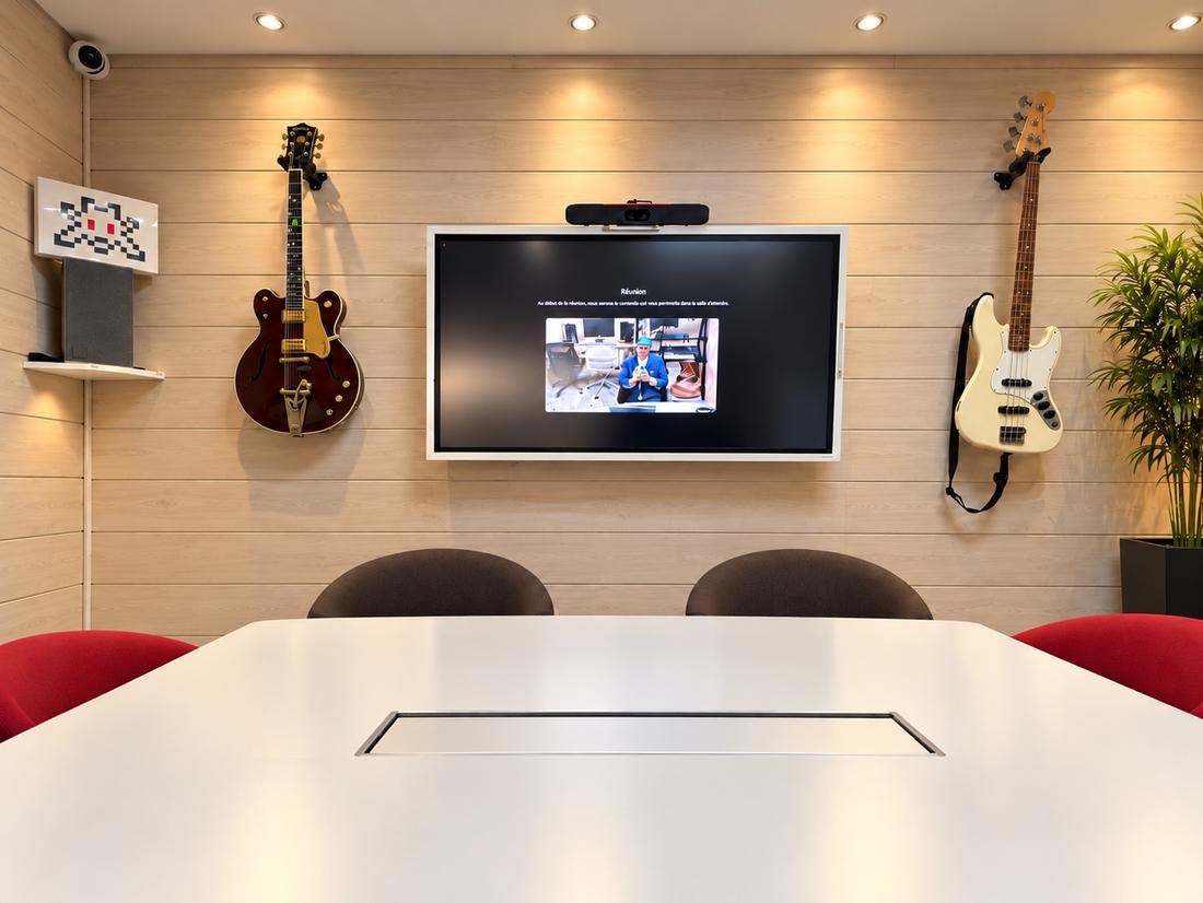 Agency meeting room: white table, video-conference screen, and a guitar and a bass hung on a light wooden wall.