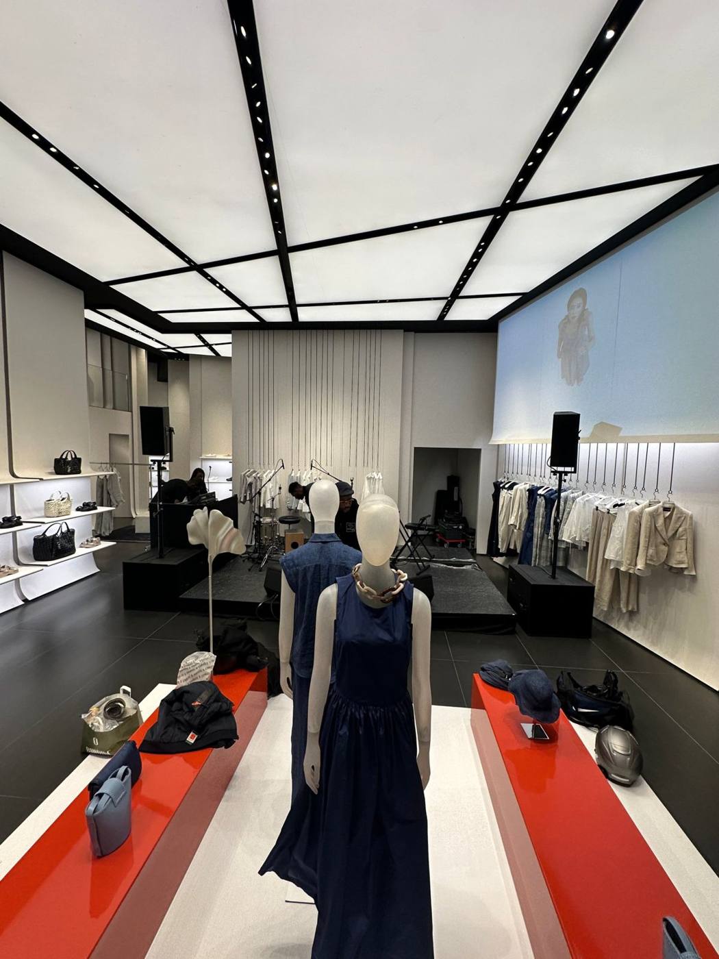 Vue de la boutique depuis l'entrée : mannequins au premier plan, scène et écran au fond.