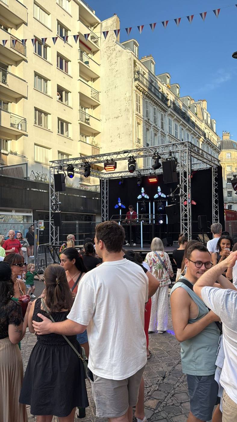 DJ sur scène devant un public massé dans la rue, structure de scène éclairée en bleu et rouge.