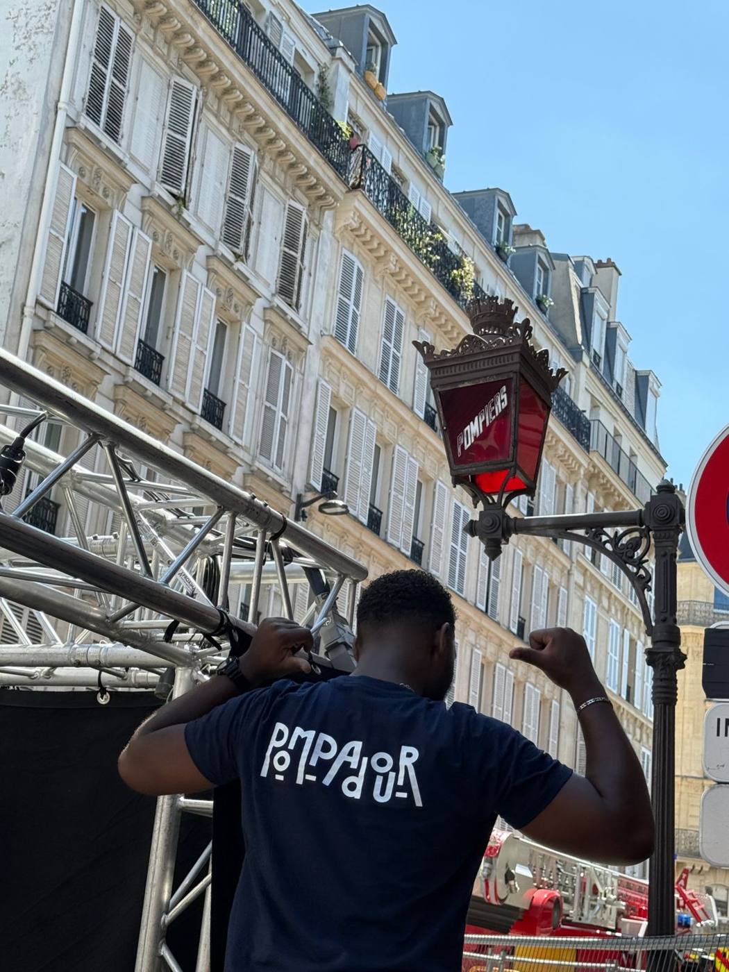 Technicien Pompadour posant devant un réverbère « Pompiers », structure de scène à gauche.