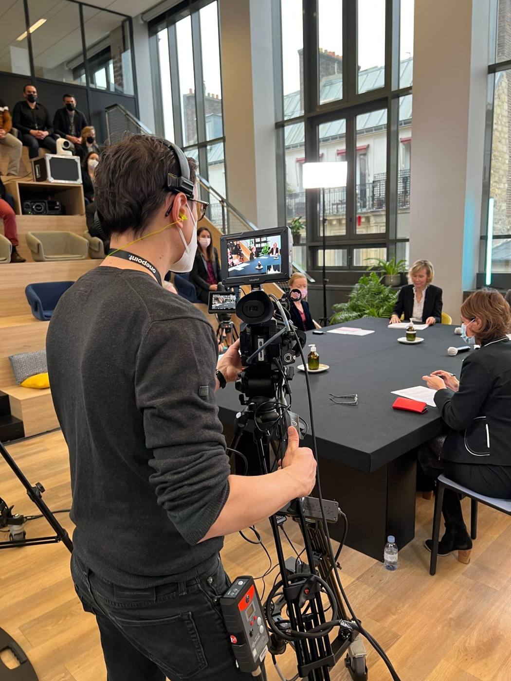 Cadreur avec caméra d'épaule devant la table des intervenants.