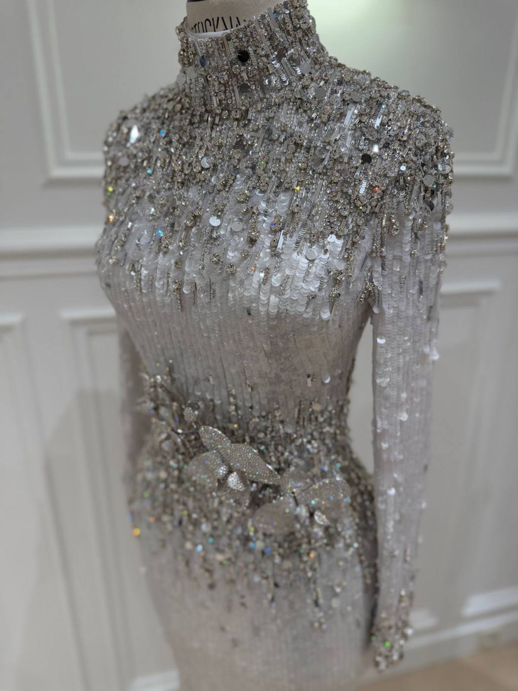 Détail d'une robe brodée de paillettes et de cristaux, avec une fleur en strass à la taille.