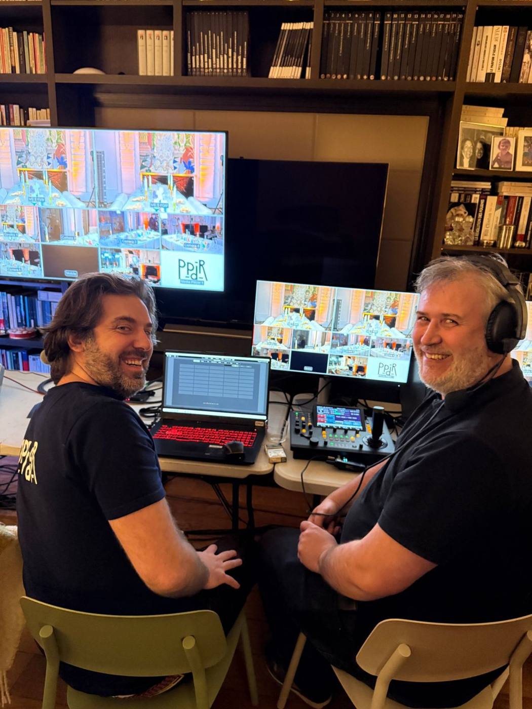 Deux techniciens souriants devant les écrans de la régie vidéo, multi-vue de huit caméras et pupitre de pilotage.