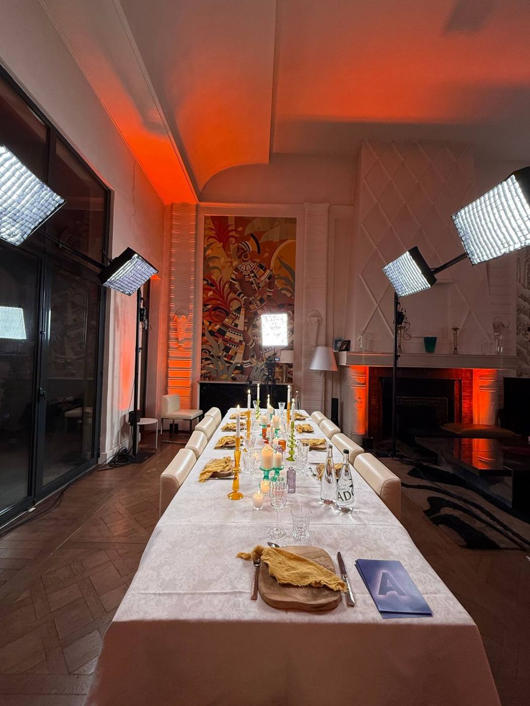 Longue table dressée aux bougies et verres colorés, salon éclairé en orange, projecteurs à LED de part et d'autre.