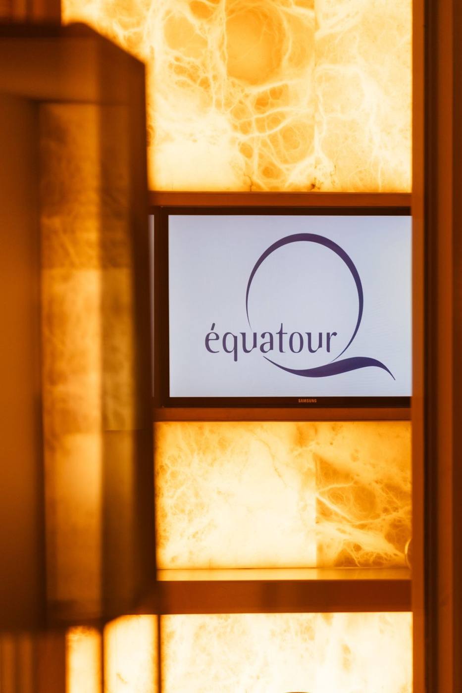 Écran affichant le logo Équatour devant un mur rétroéclairé.