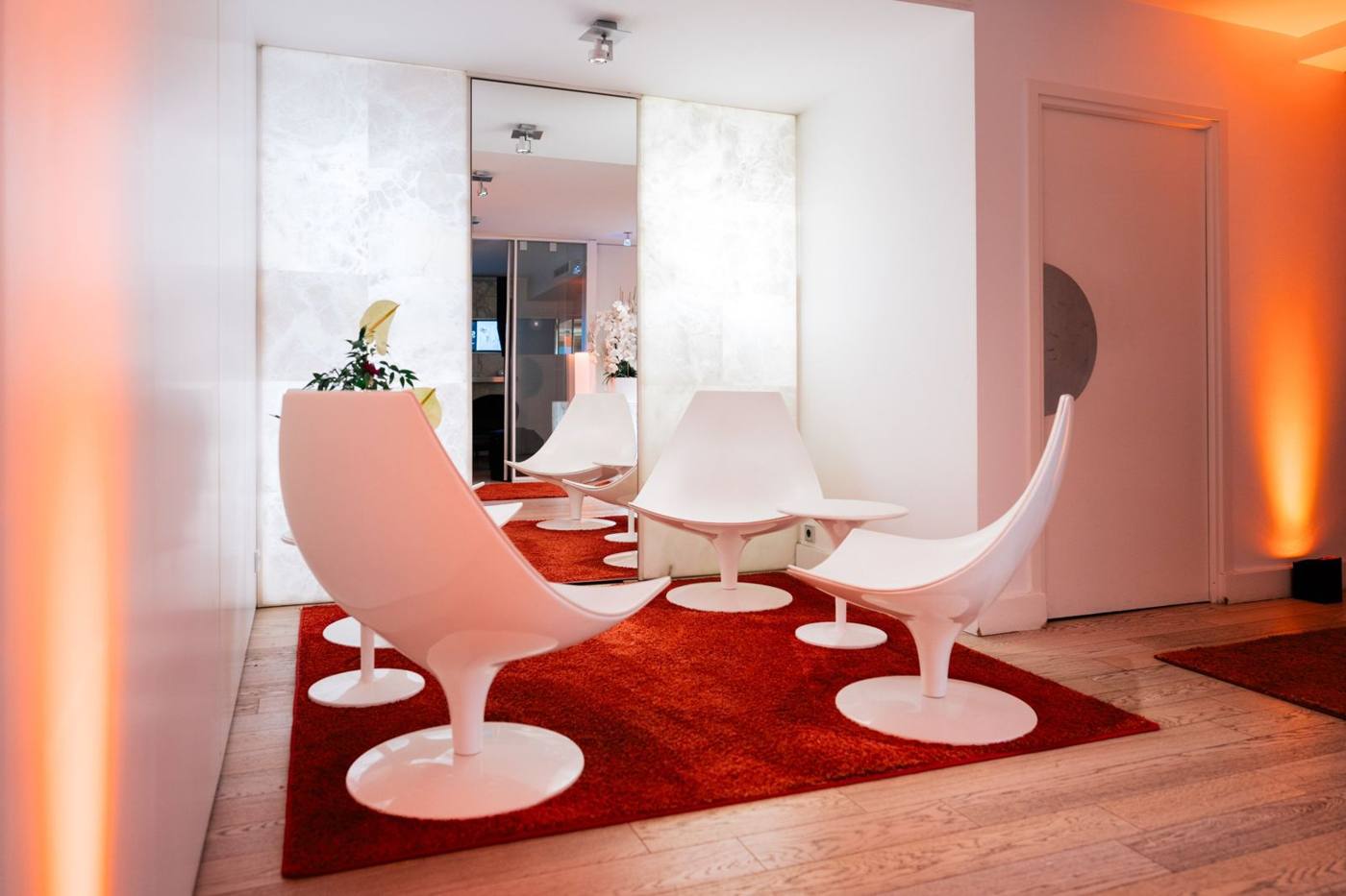Salon avec fauteuils blancs sur un tapis rouge, parois rétroéclairées et lumière orange.
