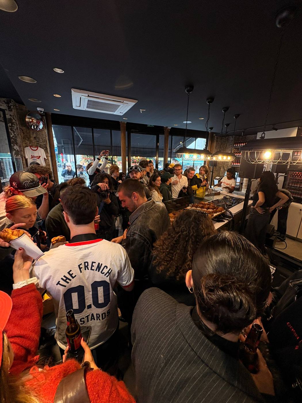 Boulangerie bondée : public, viennoiseries sur le comptoir, tee-shirt « The French Bastards 0.0 », platines au fond.