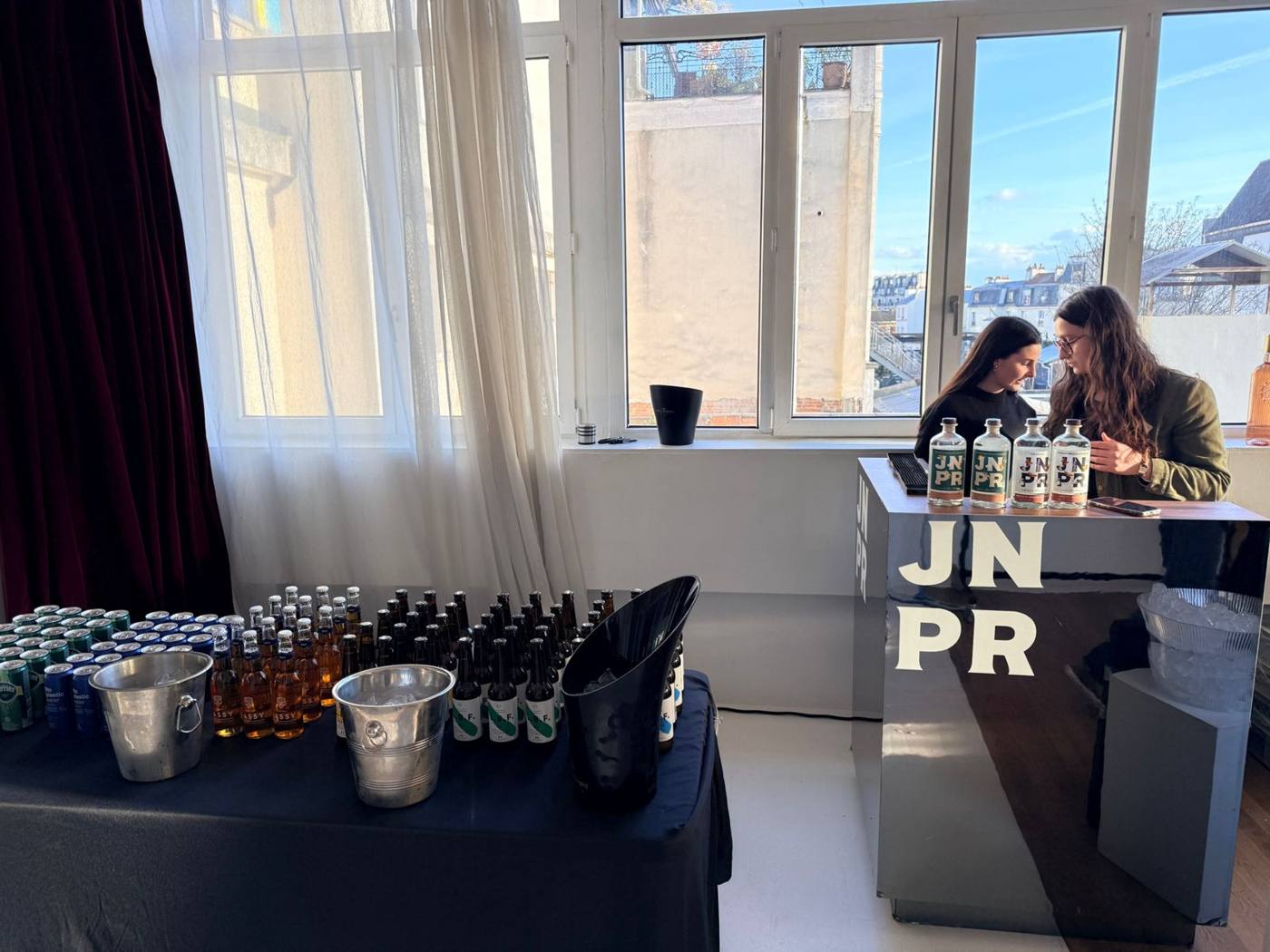 Bar JNPR et table de boissons devant de grandes fenêtres sur les toits de Paris.