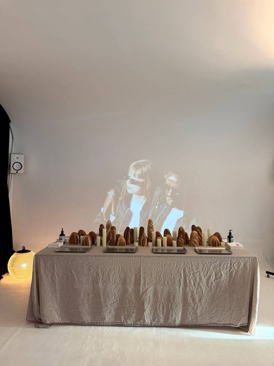 Table nappée de lin avec pains et bougies, projection de film au mur, enceinte de monitoring.