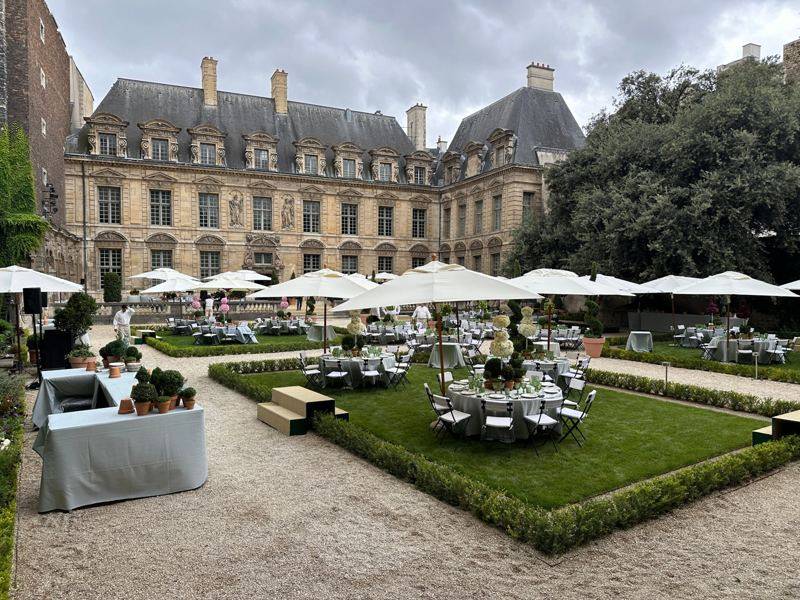 Jardin de l'hôtel particulier avec tables rondes, parasols blancs et buis taillés.