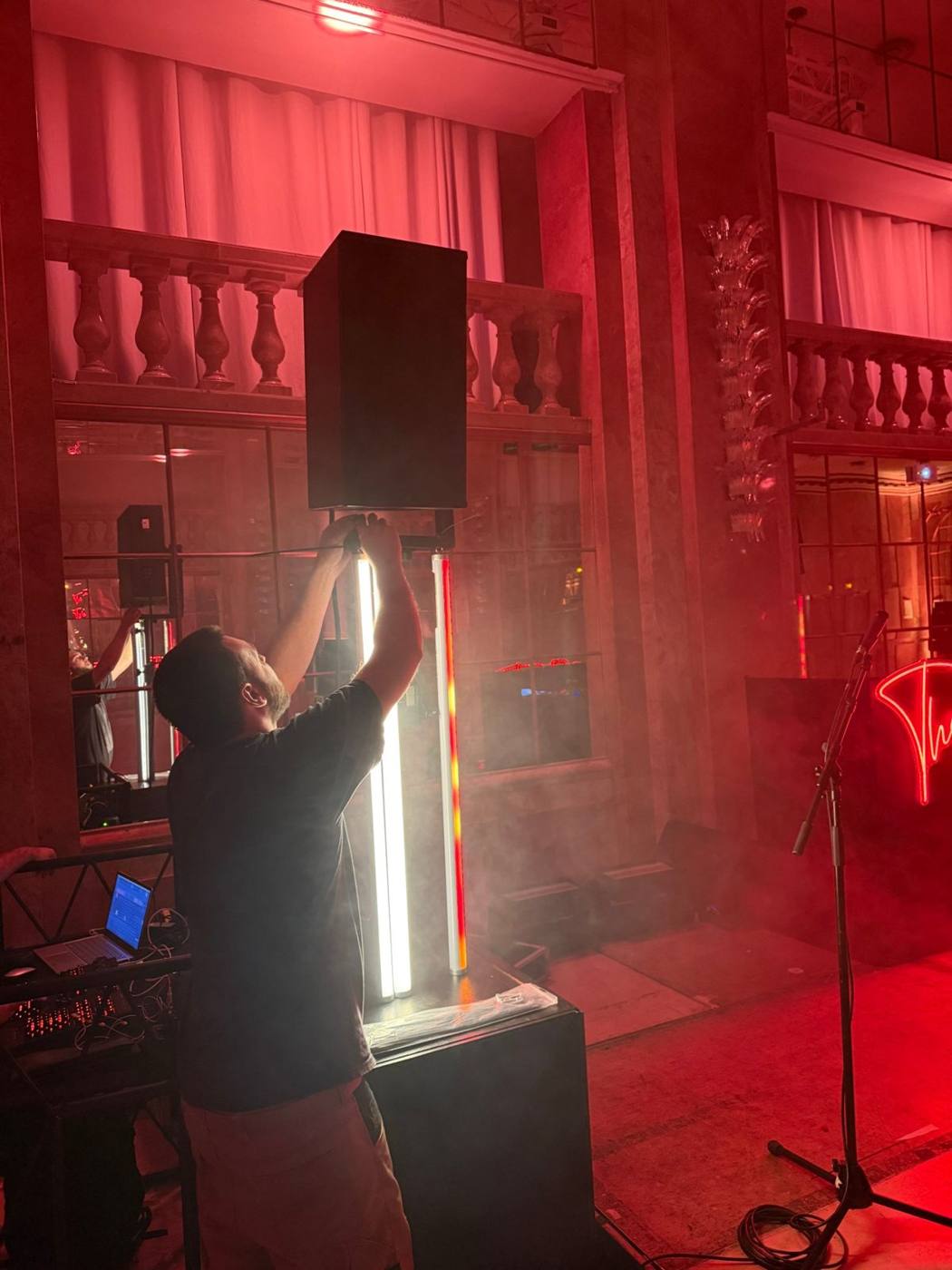 Technicien réglant une enceinte sur pied et des tubes lumineux dans la salle rouge.