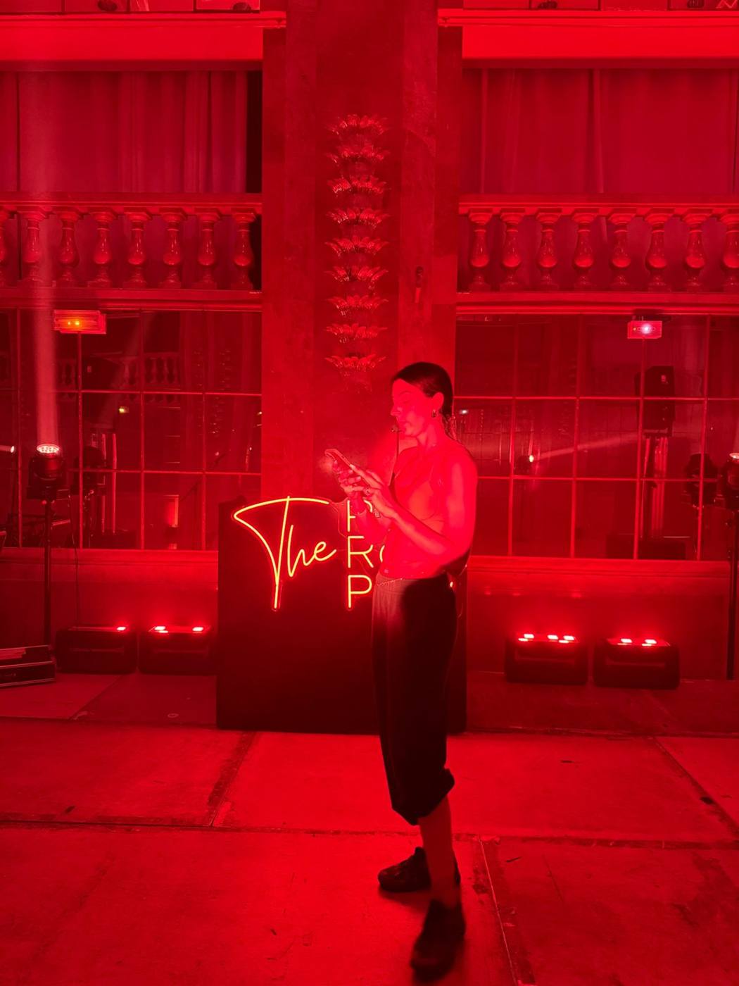 Intervenante au micro-casque devant l'enseigne néon « The Red Room Party », salle éclairée en rouge.