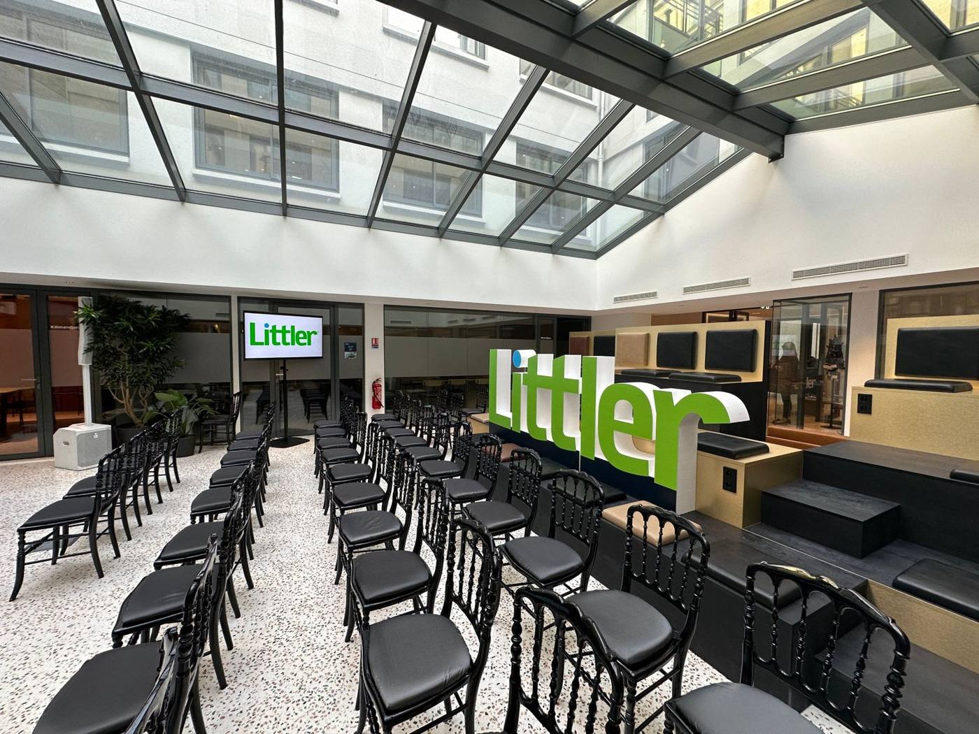 Salle installée avant l'événement : chaises noires en rangées, écran Littler et lettrage en volume.