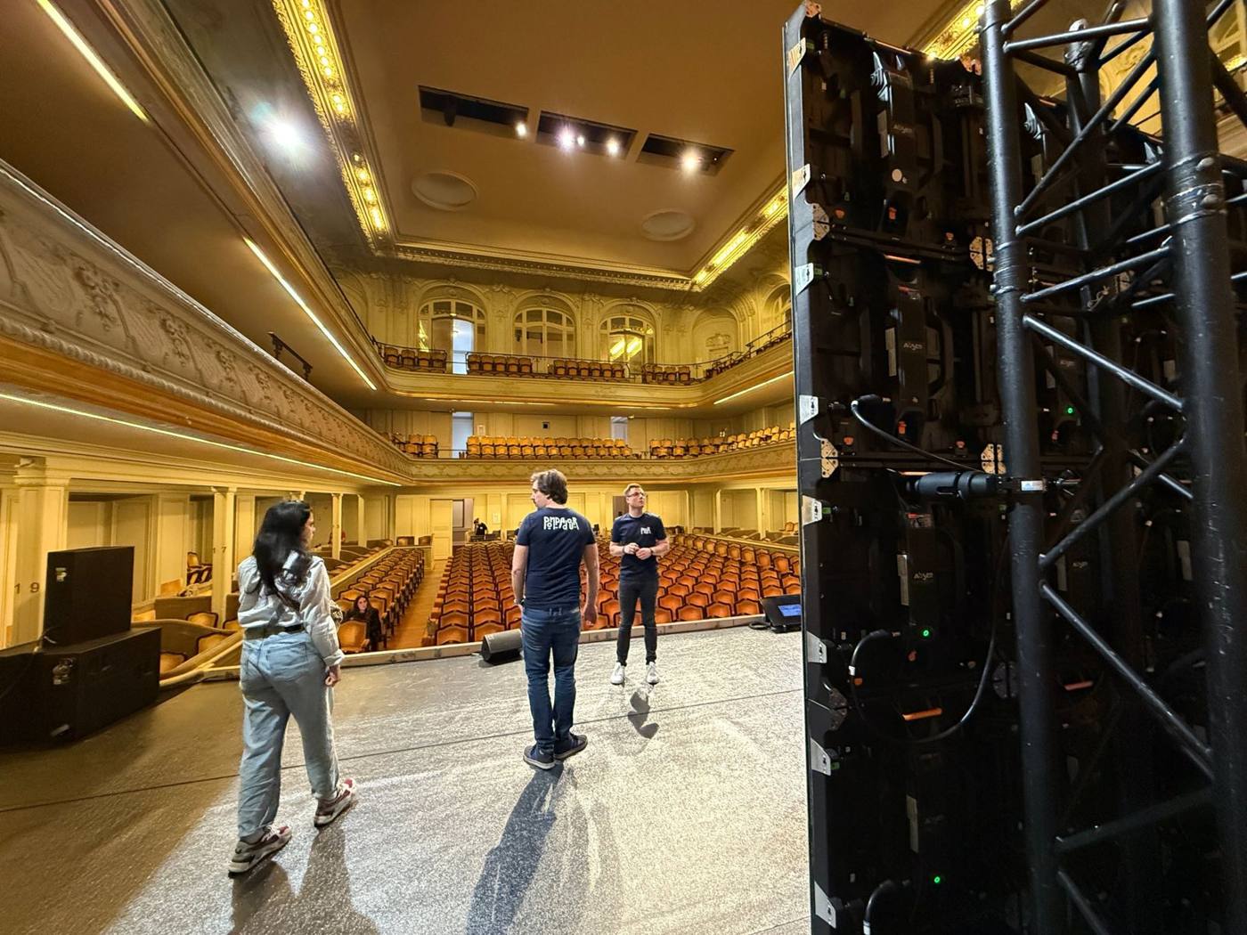 Équipe sur scène avant l'événement, face à la salle vide, mur LED en construction au premier plan.