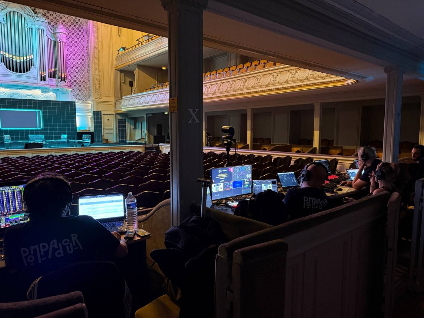 Régie installée au balcon : écrans multi-vue, ordinateurs, techniciens casqués, scène et orgue en vue.