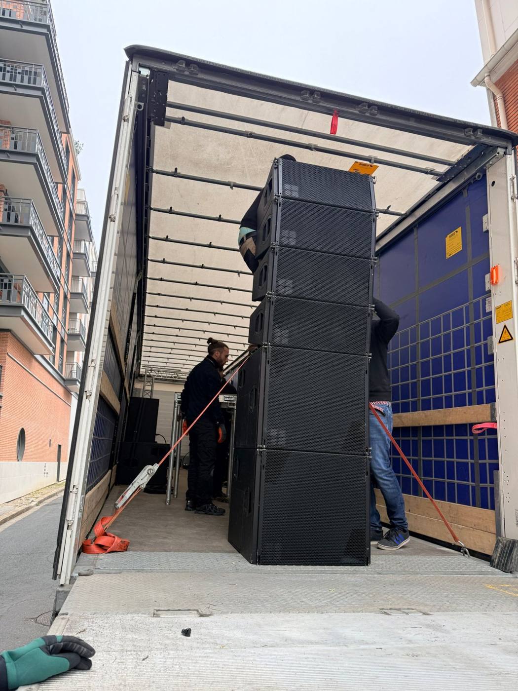 Installation d'un line array dans le semi-remorque, deux techniciens et sangles orange.