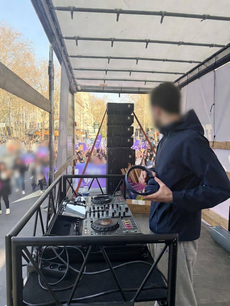 DJ au casque derrière la console de mixage sur le plateau, line array et cortège en arrière-plan.