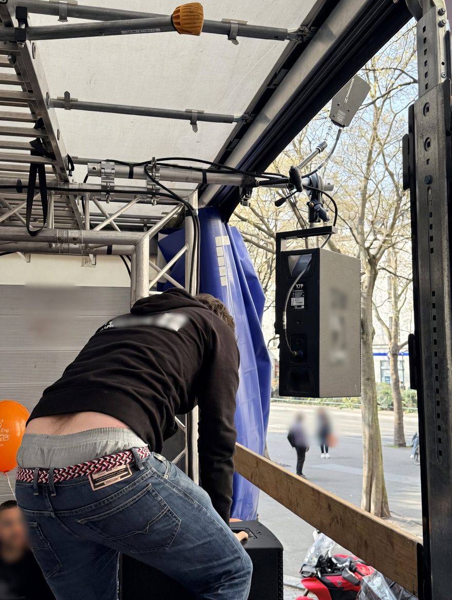 Technicien penché sur le plateau du camion, enceinte suspendue à la structure en aluminium.