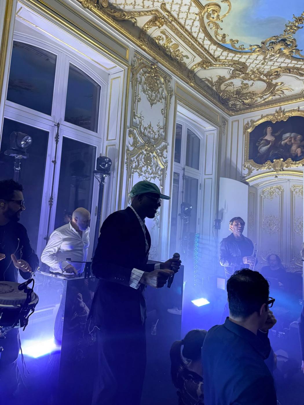 Chanteur au micro devant le DJ et un trompettiste, salon aux boiseries dorées.