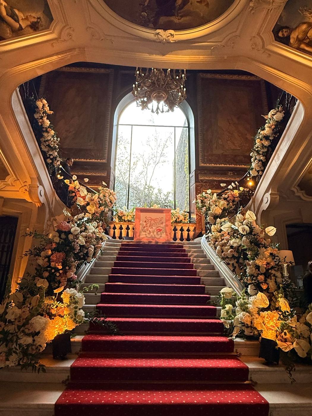 Escalier d'honneur au tapis rouge orné de fleurs blanches et pêche.