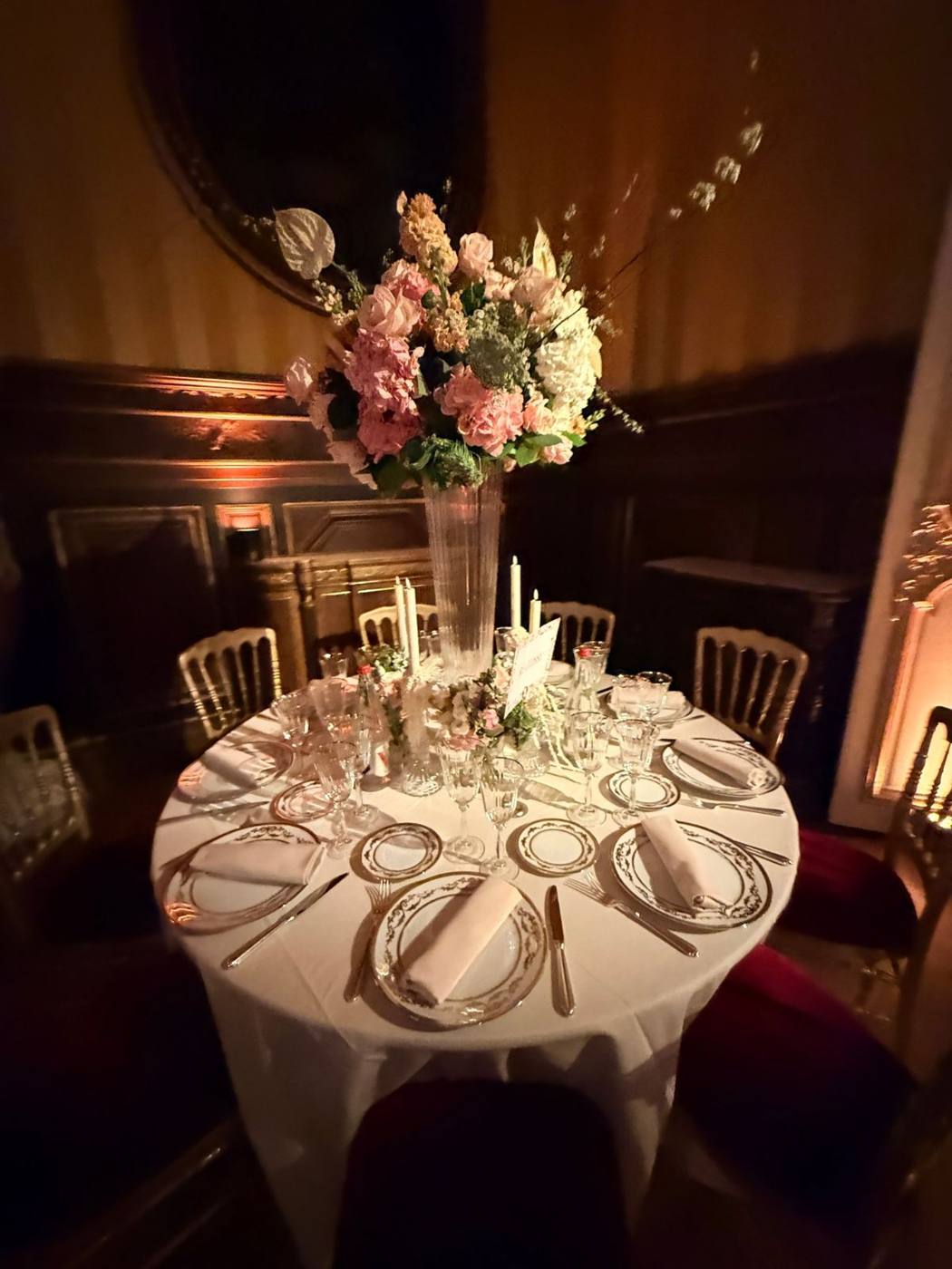 Table ronde dressée, centre de table fleuri et chandelles, chaises dorées.