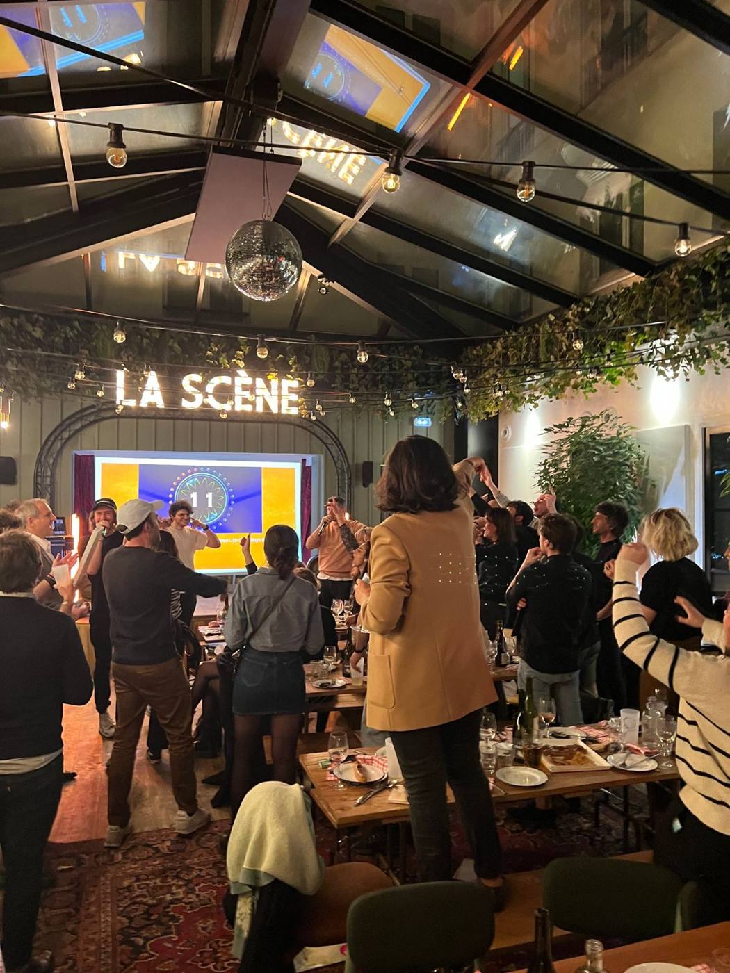 Soirée sous la verrière : invités debout et intervenants au micro devant l'écran.