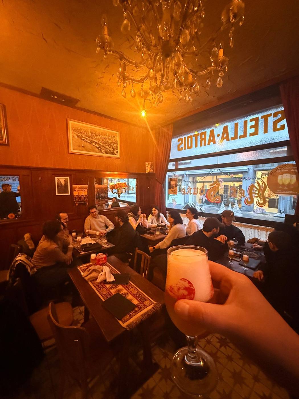 Salle de bar aux boiseries sous un lustre, enseigne lumineuse en vitrine, coupe tenue au premier plan.