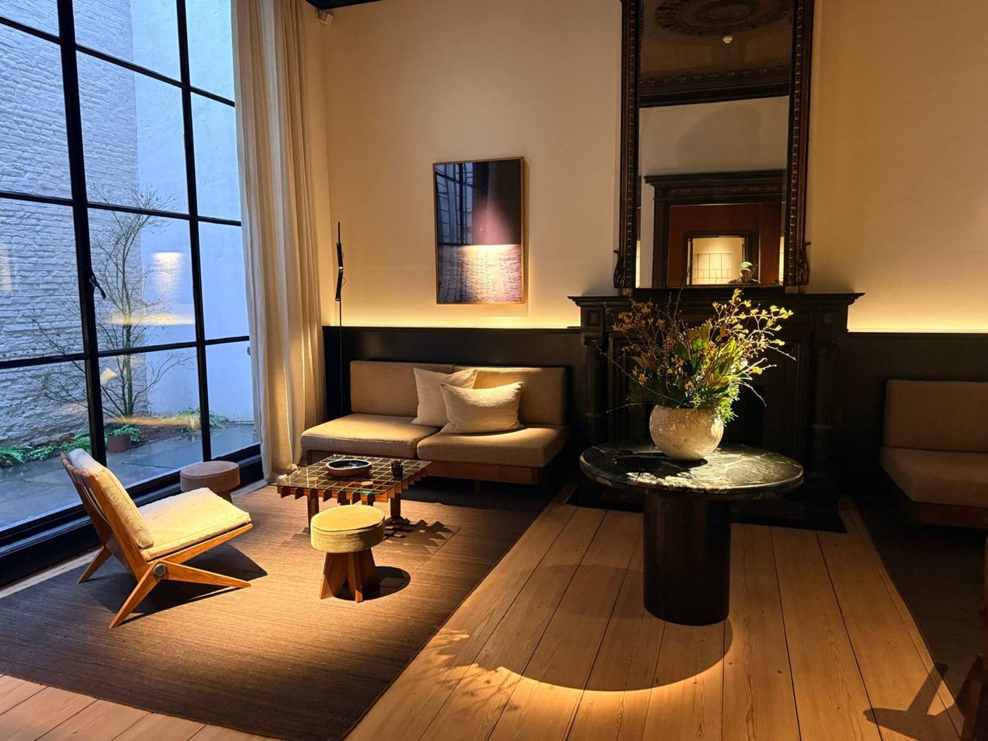 Salon aux grandes verrières d'atelier, fauteuils en bois, table basse en verre et bouquet sur table en marbre noir.