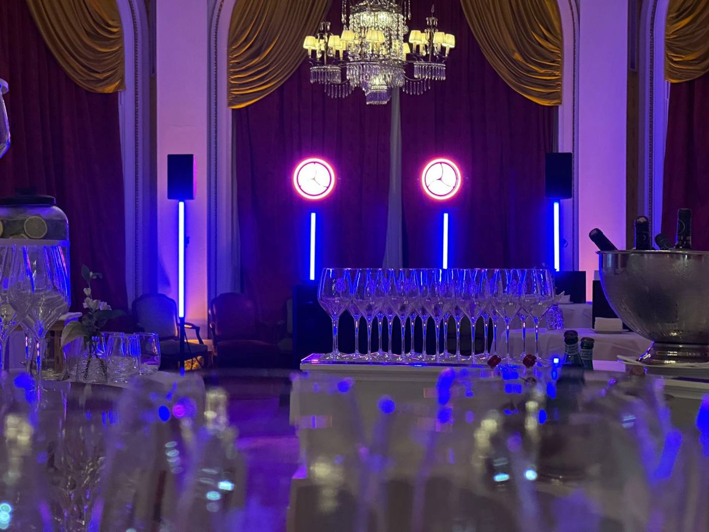 Réception dans un salon à lustre : rangée de verres, projecteurs en cercle et tubes lumineux bleus.