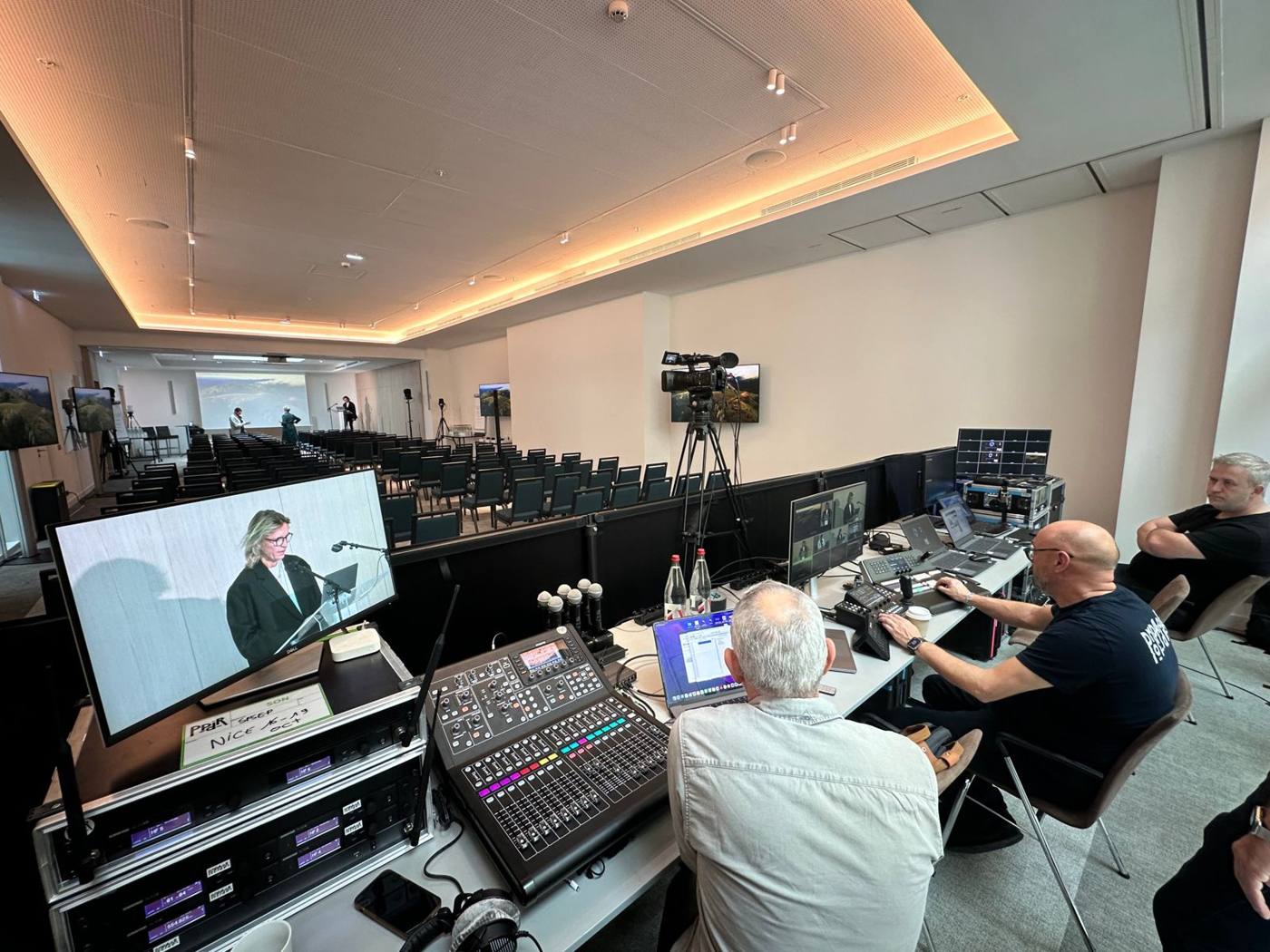 Régie son et vidéo : console de mixage, micros HF, moniteur de retour sur l'intervenante au pupitre.