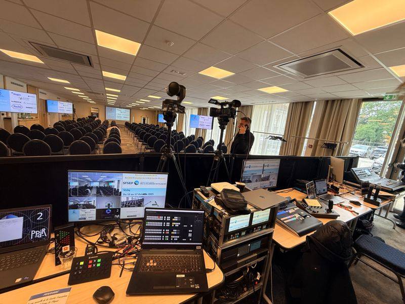Régie vidéo et son devant une salle de conférence : moniteur multi-vue, mélangeur Blackmagic ATEM, caméra motorisée et caméra d'épaule sur pied.