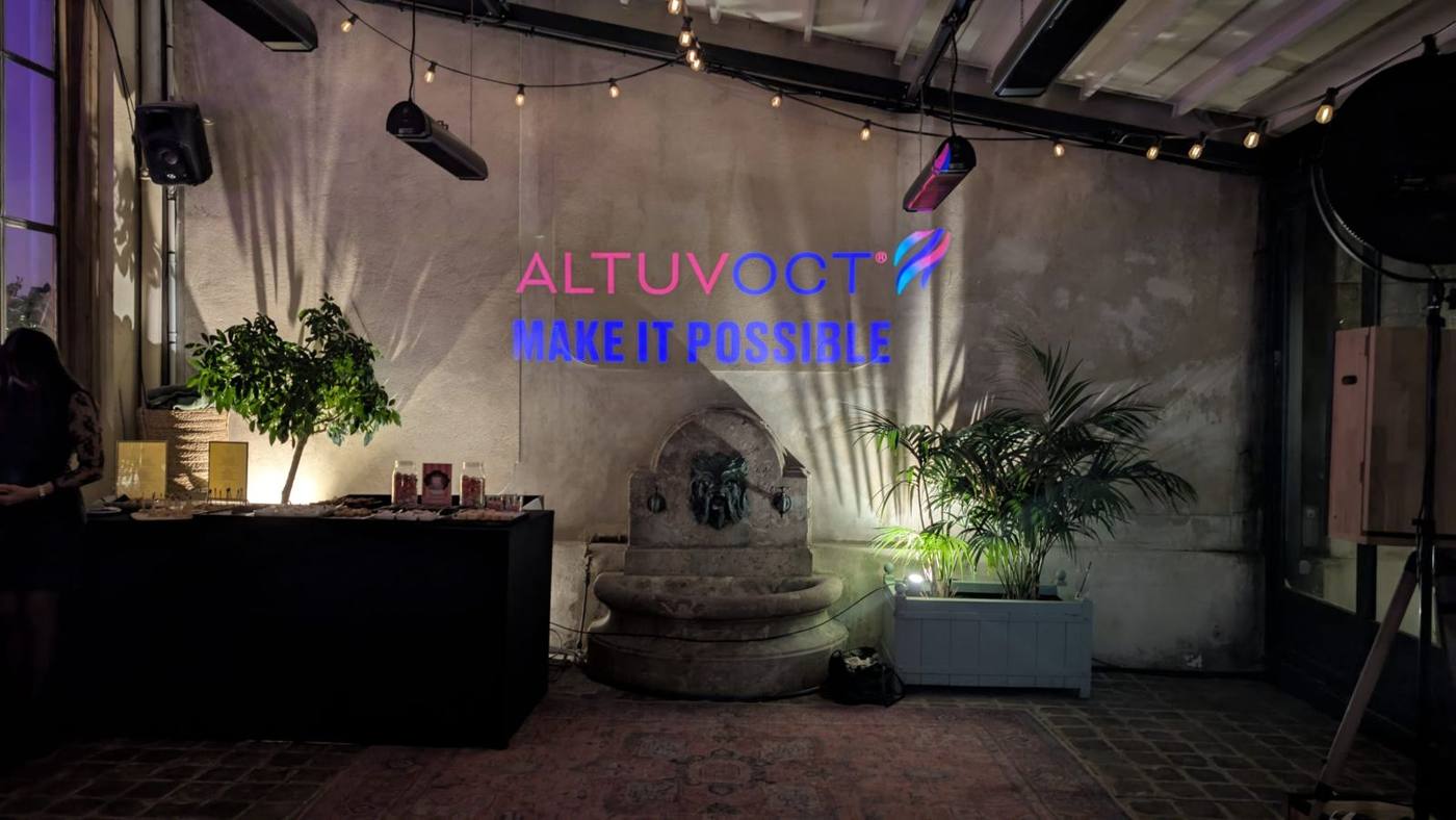 Logo projeté sur un mur de pierre par un projecteur à gobo, buffet noir et plantes, guirlandes lumineuses.