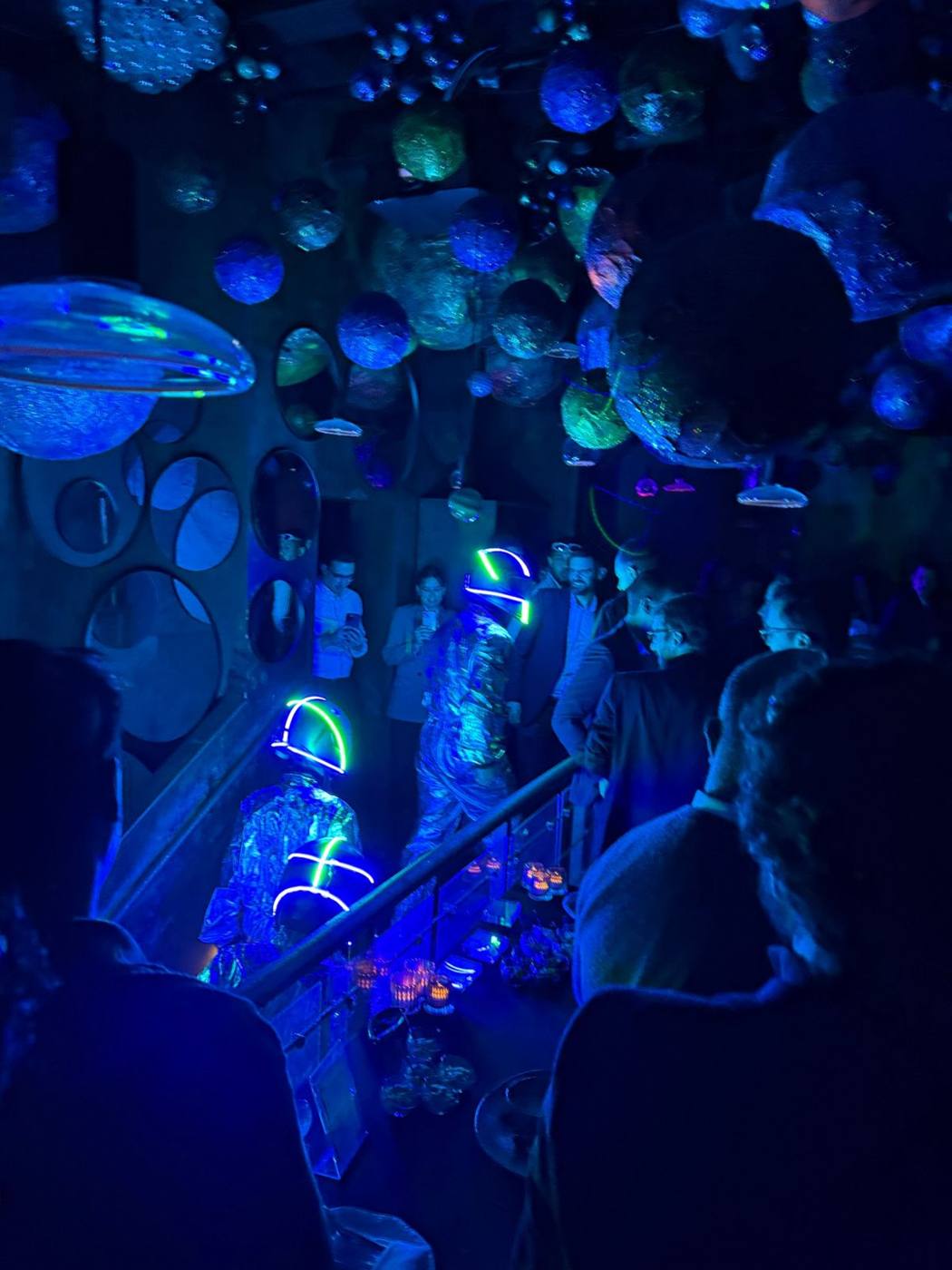 Deux astronautes en combinaison argentée aux casques lumineux, au milieu des invités.