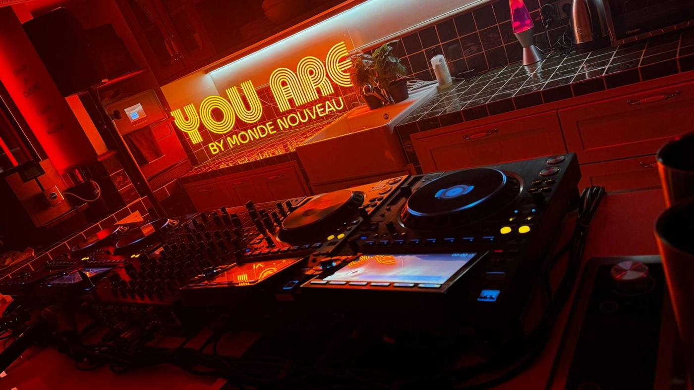 Platines et mixeur DJ sur un plan de travail carrelé, devant le néon « You are by Monde Nouveau ».