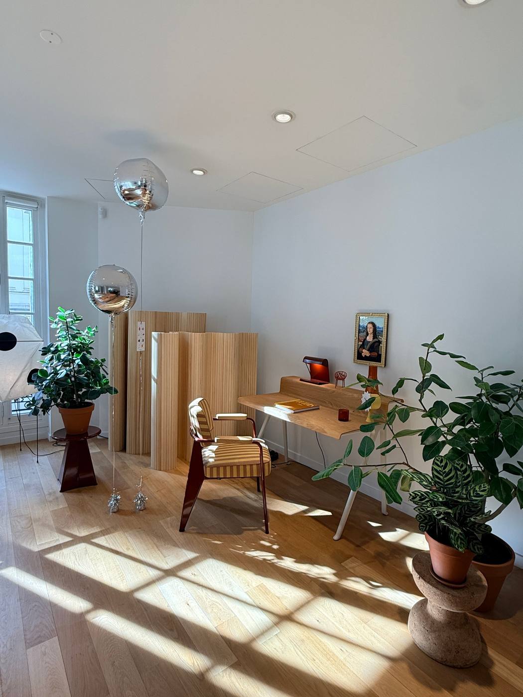 Coin bureau avec fauteuil rayé, paravent en bois, ballons argentés et plantes.
